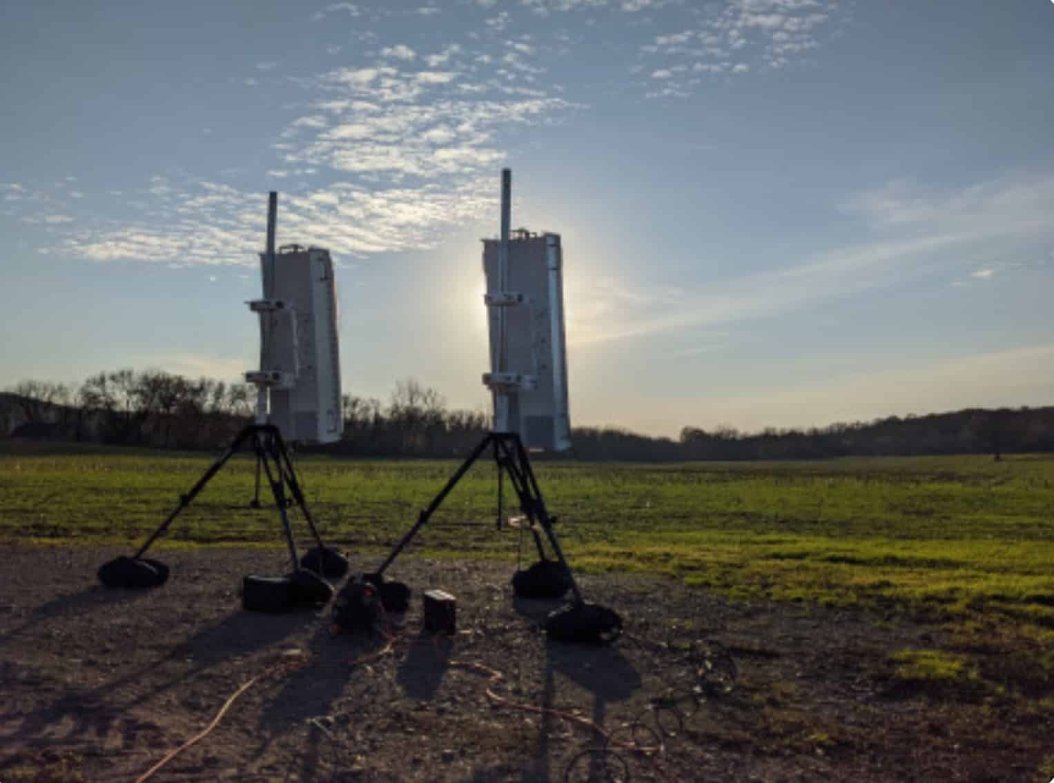 Two sensor units stand on tripods in an open field at sunset.