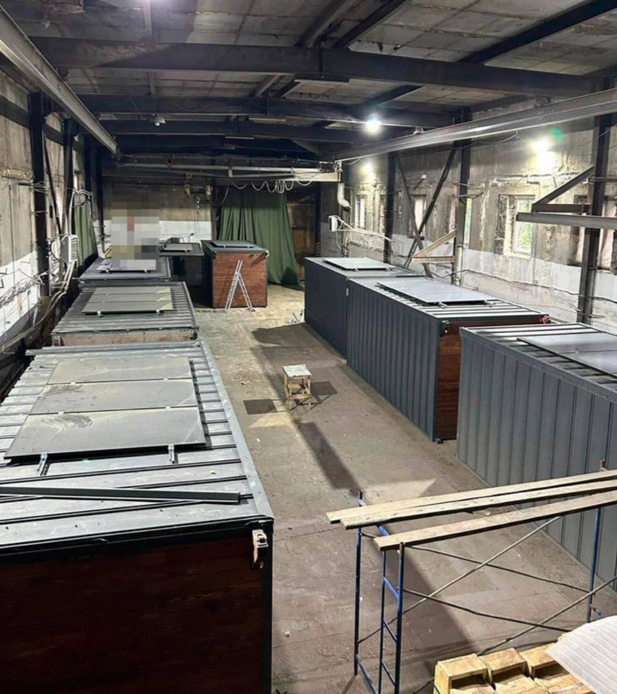 Shipping containers with their roof panels removed stand inside an empty industrial shed.