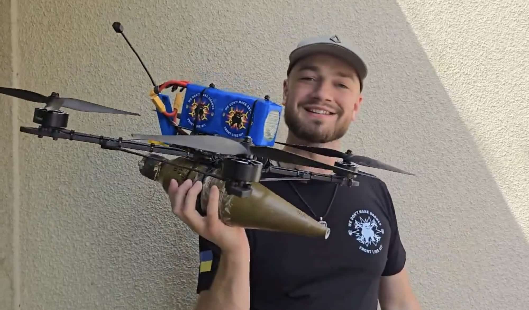 A man holds a hexacopter fitted with an improvised munition under its frame.