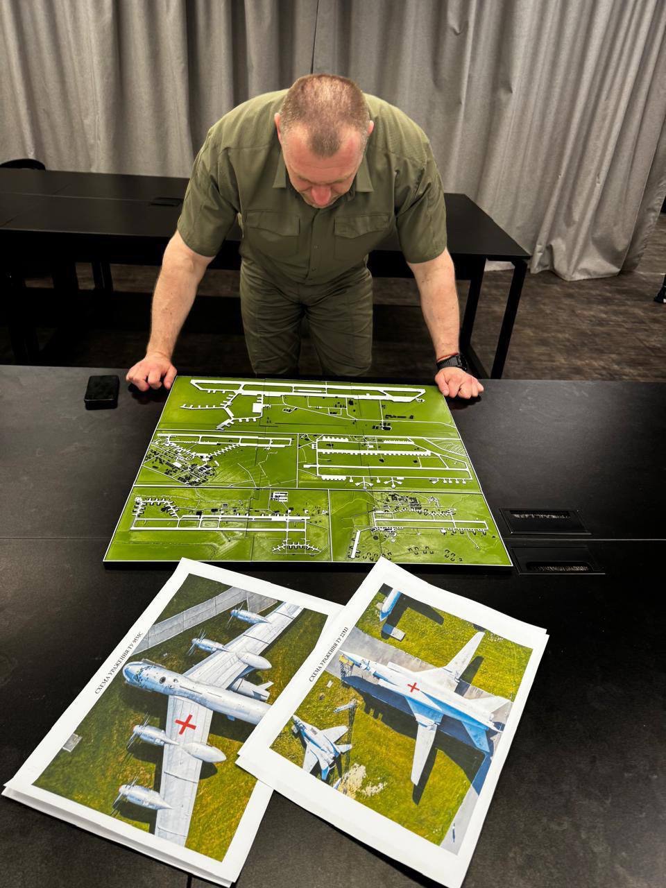 An officer in olive uniform leans over a scale model of a Russian airbase.