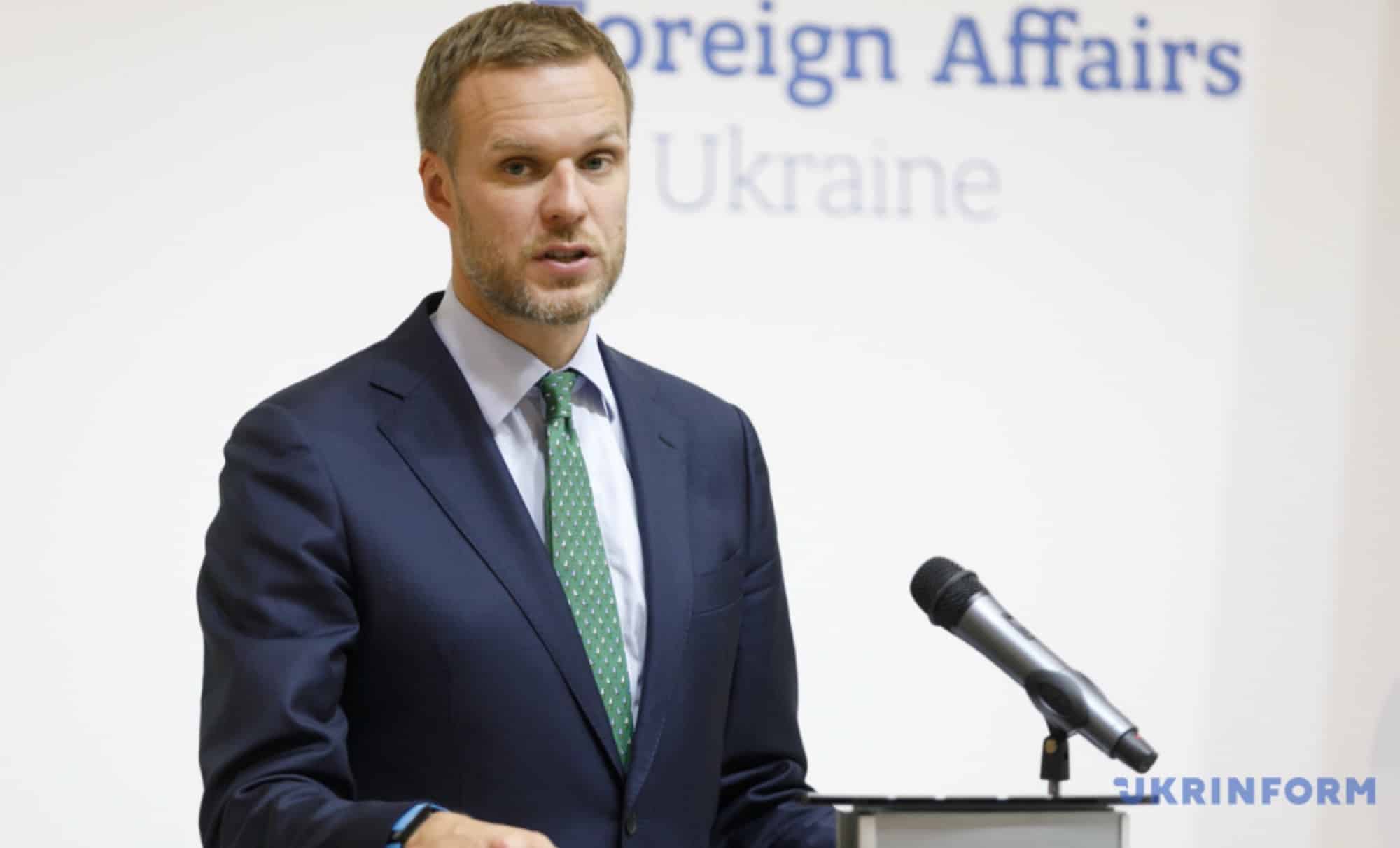 Suited official speaking at a lectern before a Ukraine foreign affairs backdrop.