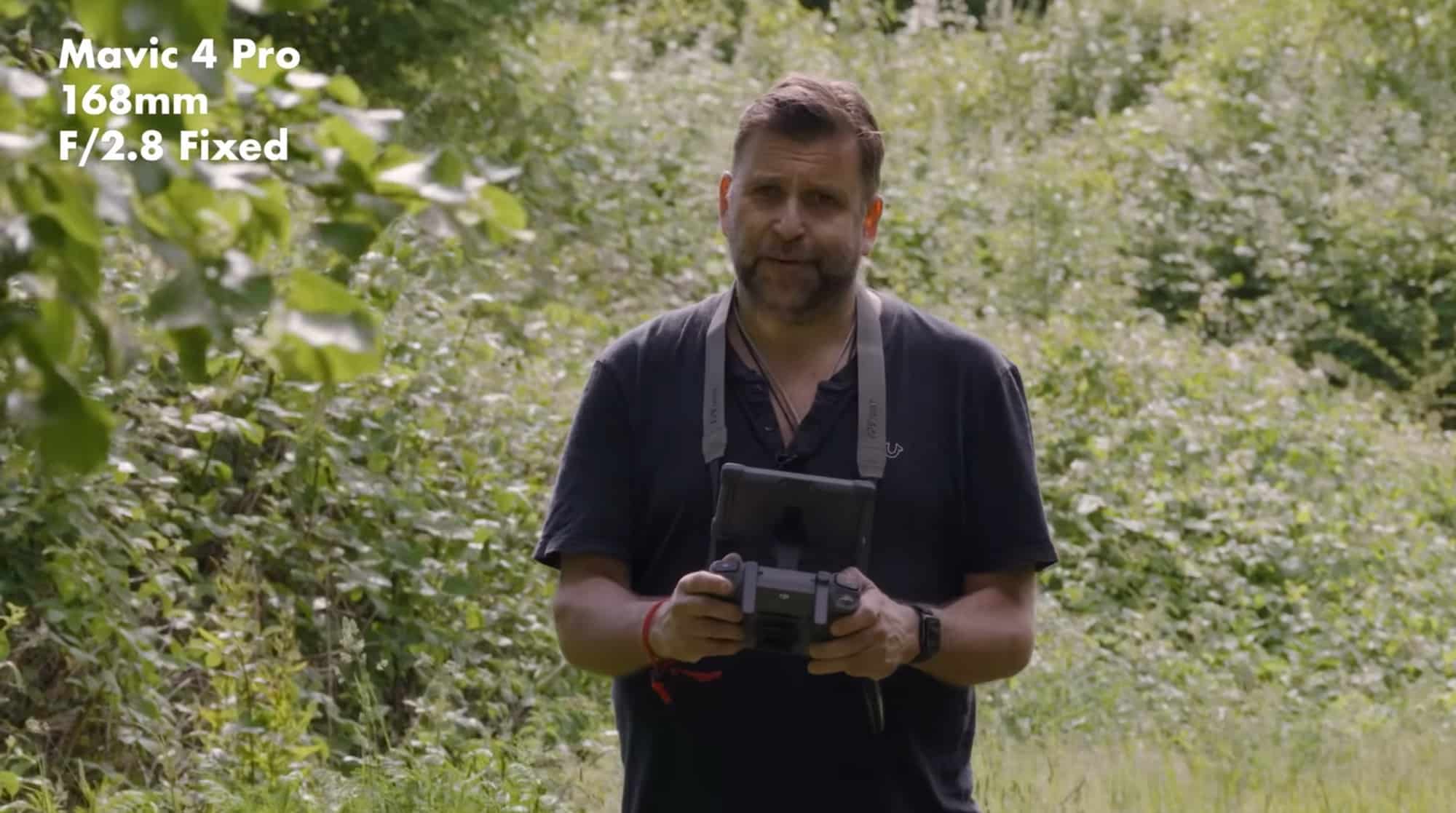 Reviewer holds a controller in a leafy field, framed by a 168mm telephoto lens.
