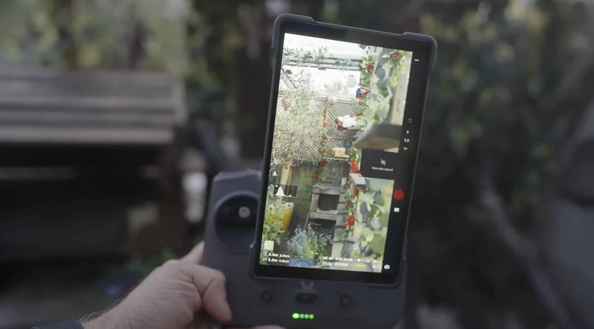 Hand holds the controller showing a live garden view on its bright screen.