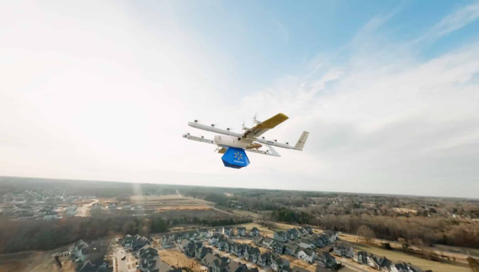 Delivery drone carries a blue Walmart parcel high above a suburban neighborhood.