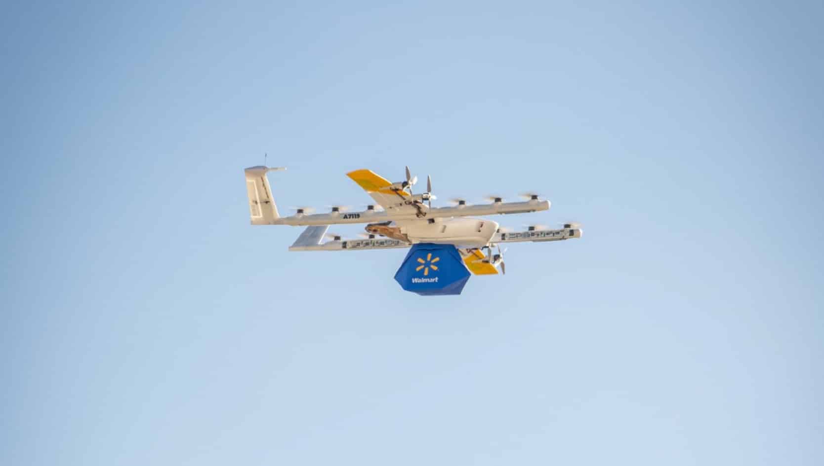 Fixed-wing delivery drone against clear sky with a Walmart package slung below.