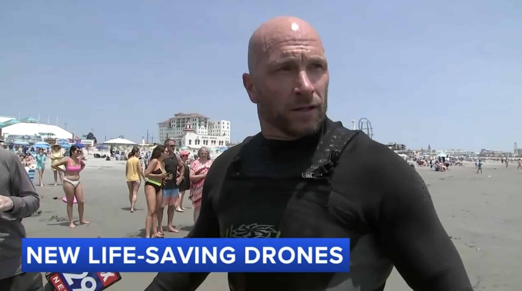 Rescue swimmer in a wetsuit standing on a crowded Ocean City beach.