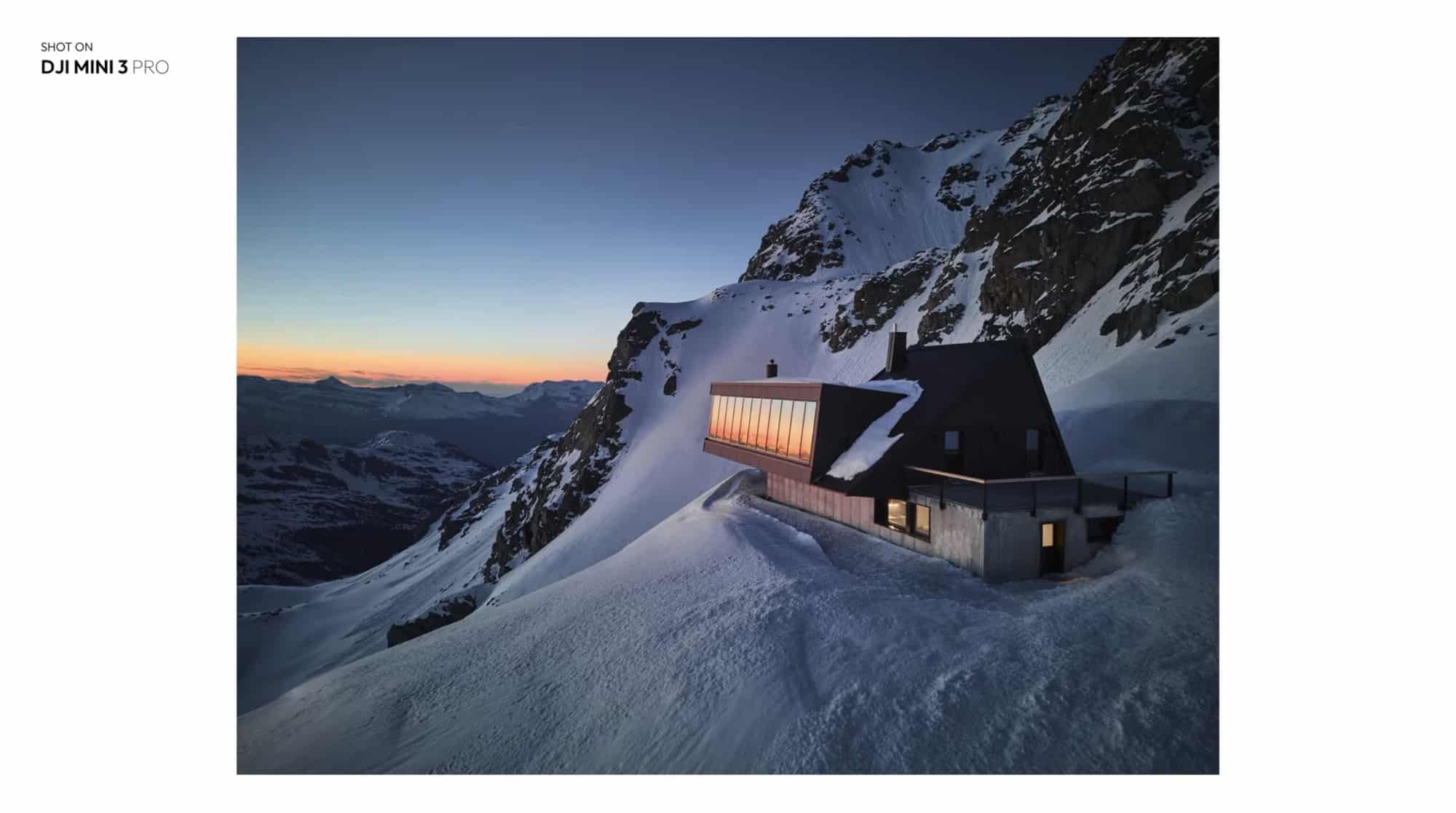 Dark mountain lodge perched on a snowy ridge at sunset, credited to the Mini 3 Pro.