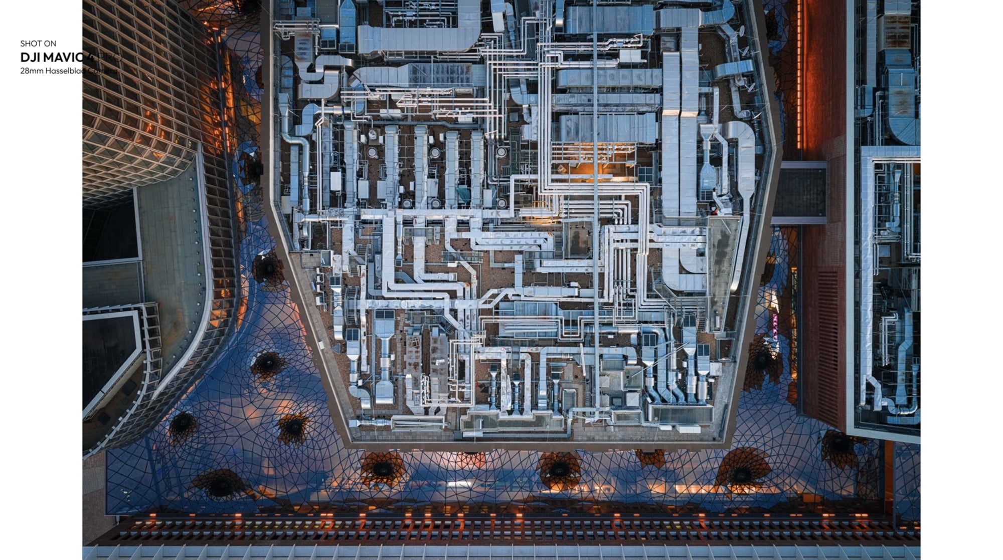 Top-down dusk aerial of a curved rooftop terrace and its lattice canopy.