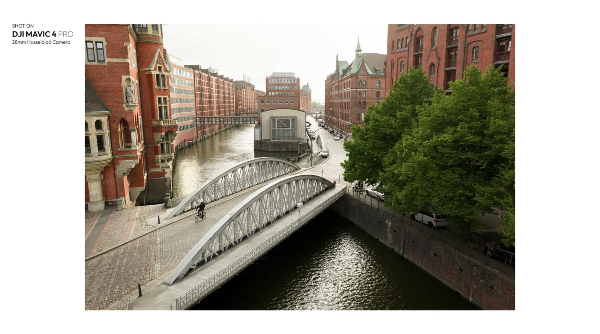 Aerial over a white steel arch bridge spanning a Speicherstadt canal.