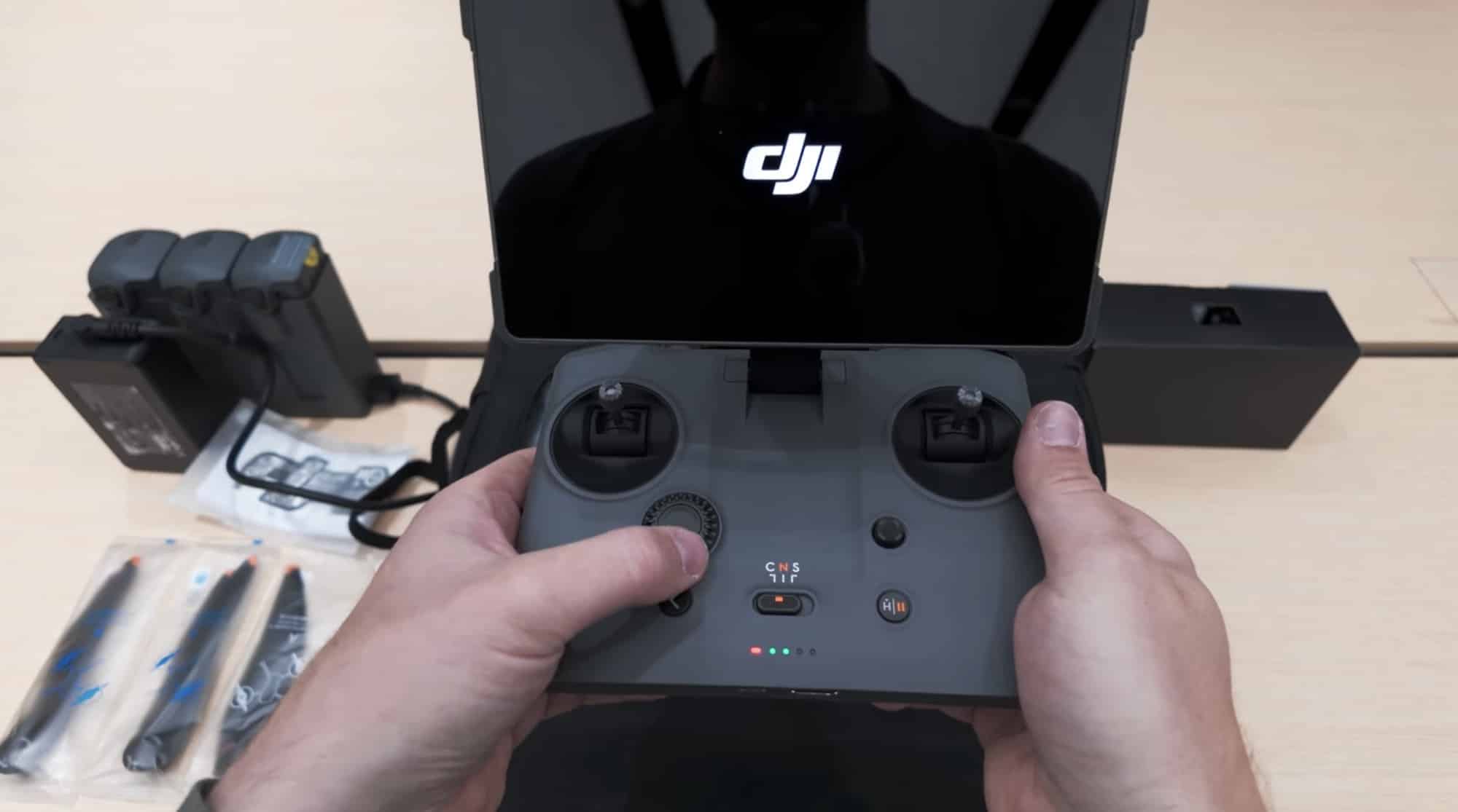 Hands gripping the RC2 Pro controller beside batteries, a charging hub and spare sticks.