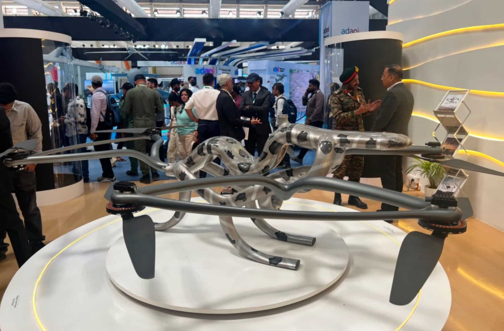 Multirotor airframe on a display stand at a crowded defence trade show.