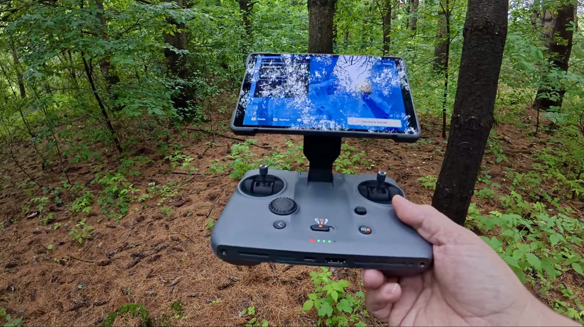 Hands holding the RC Pro 2 in woodland with an aerial view on its seven-inch screen.