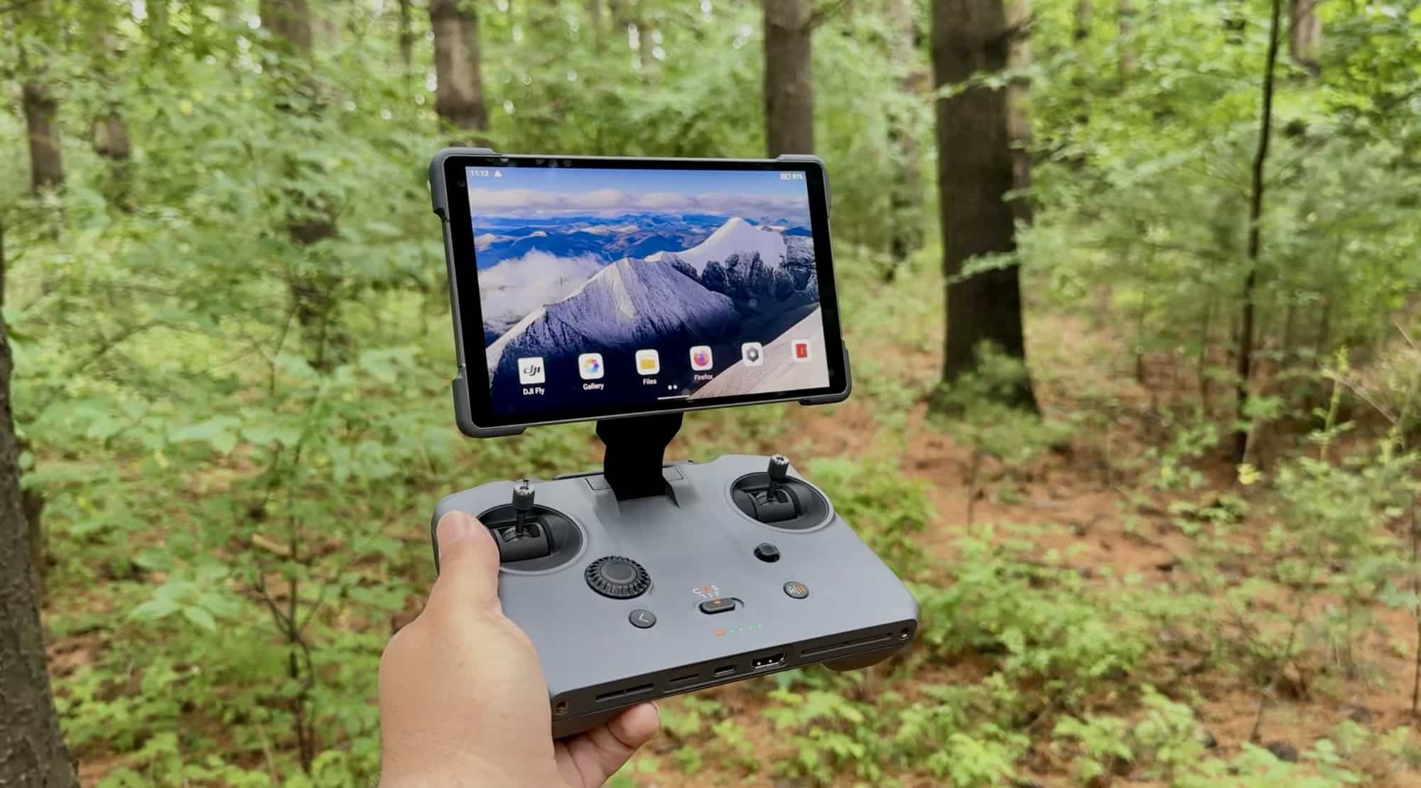 The RC Pro 2 held at waist height among trees, a mountain scene filling the display.