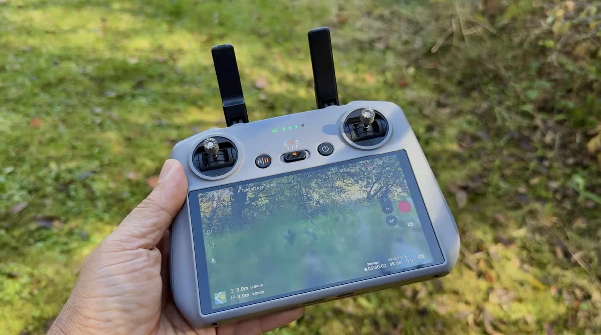 The smaller DJI RC 2 held in one hand with both antennas raised in the forest.