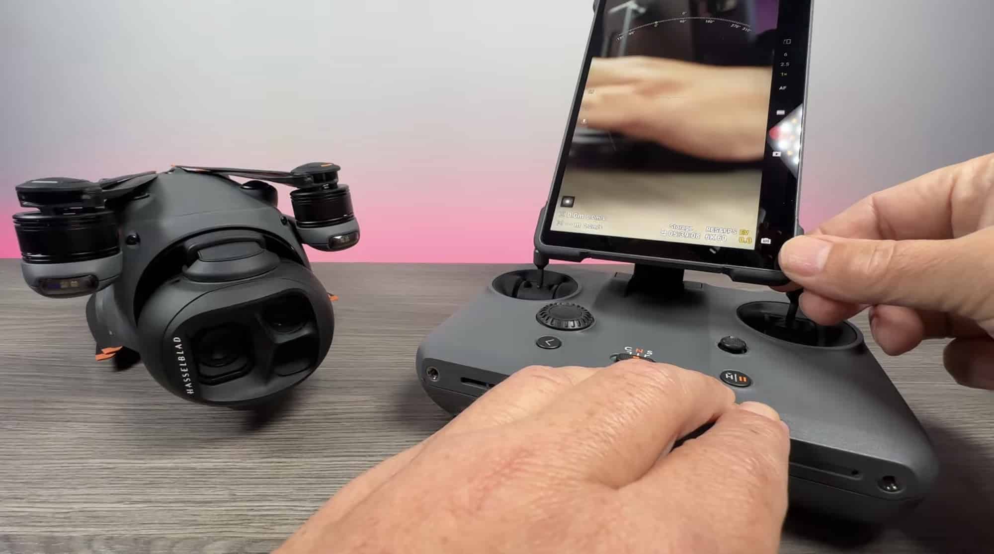 Hands working the RC Pro 2 on a wooden table beside a folded DJI drone.