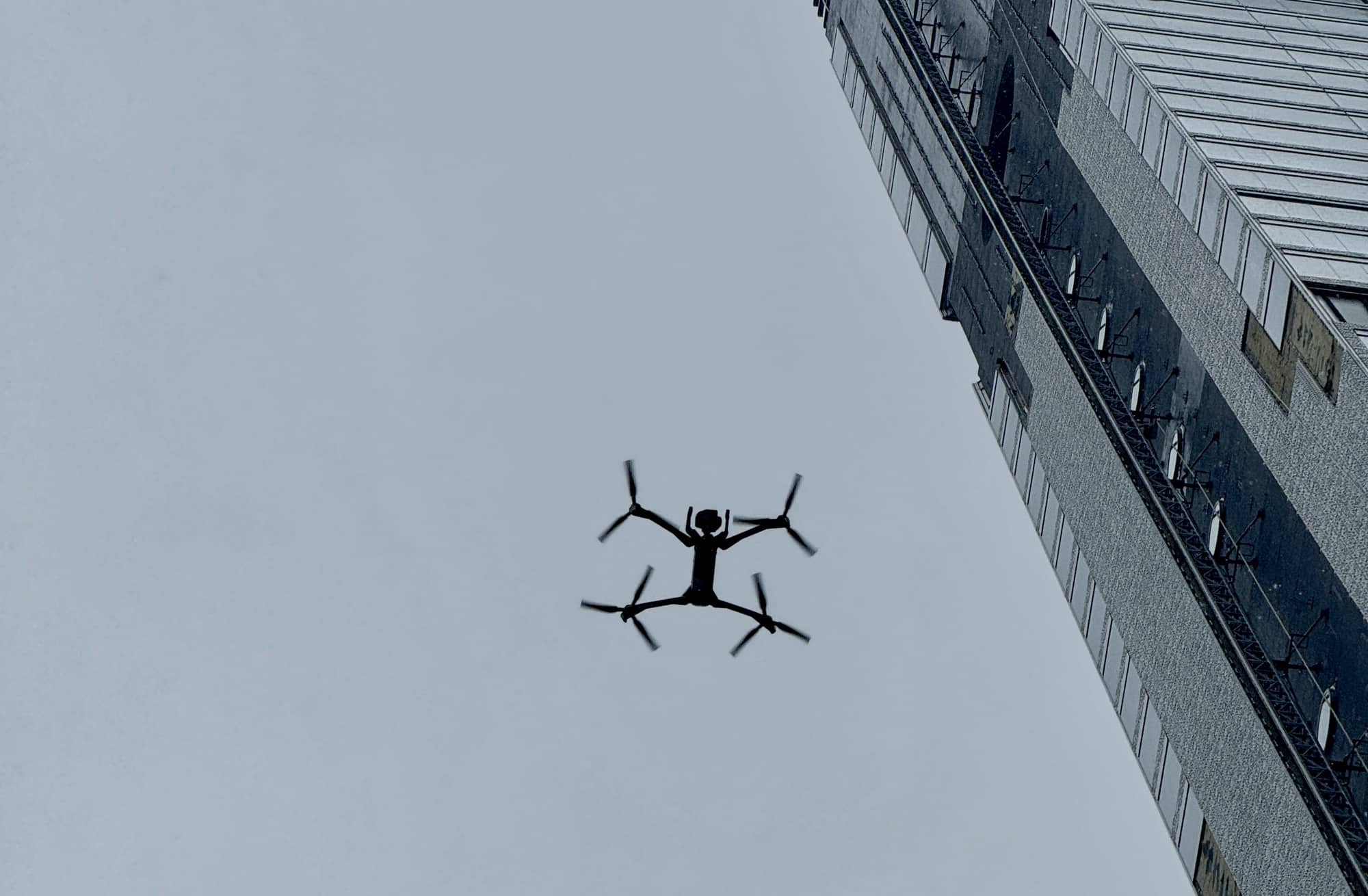 Skydio X10 hovering in gray sky beside a Manhattan high-rise facade.