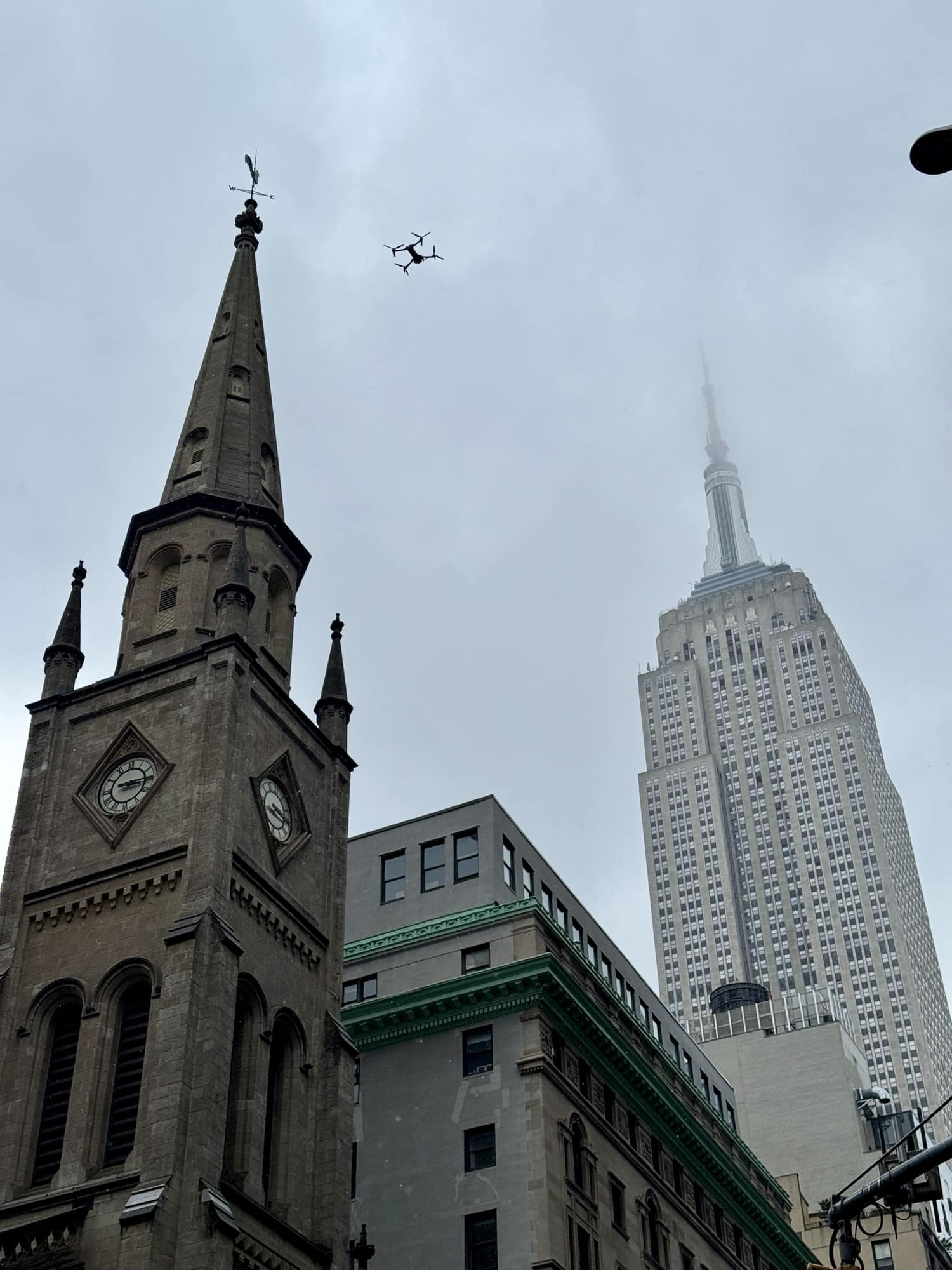 Drone circling above a church spire with the Empire State Building behind it.