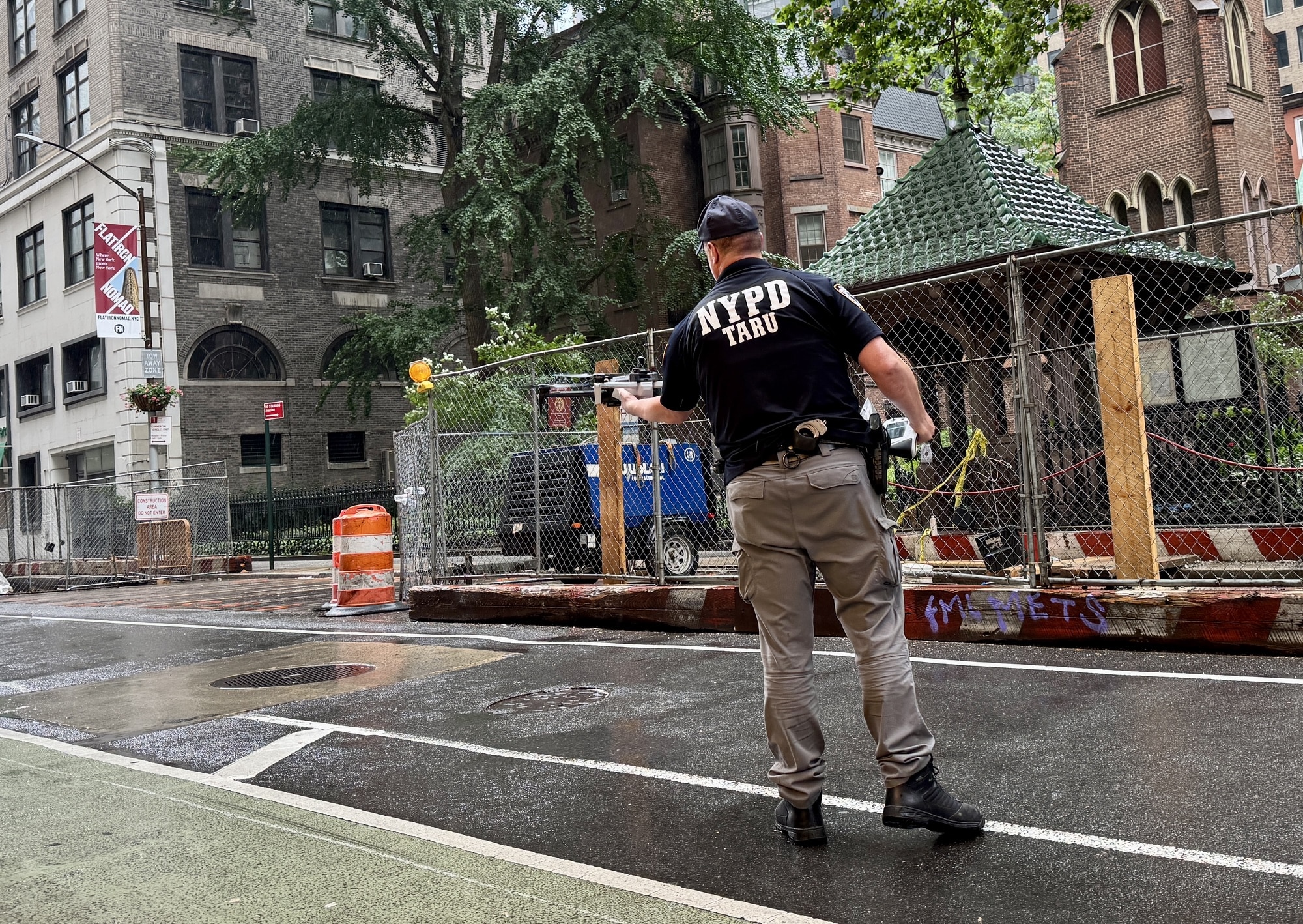 Officer in an NYPD TARU shirt walking across a rain-soaked Fifth Avenue crosswalk.