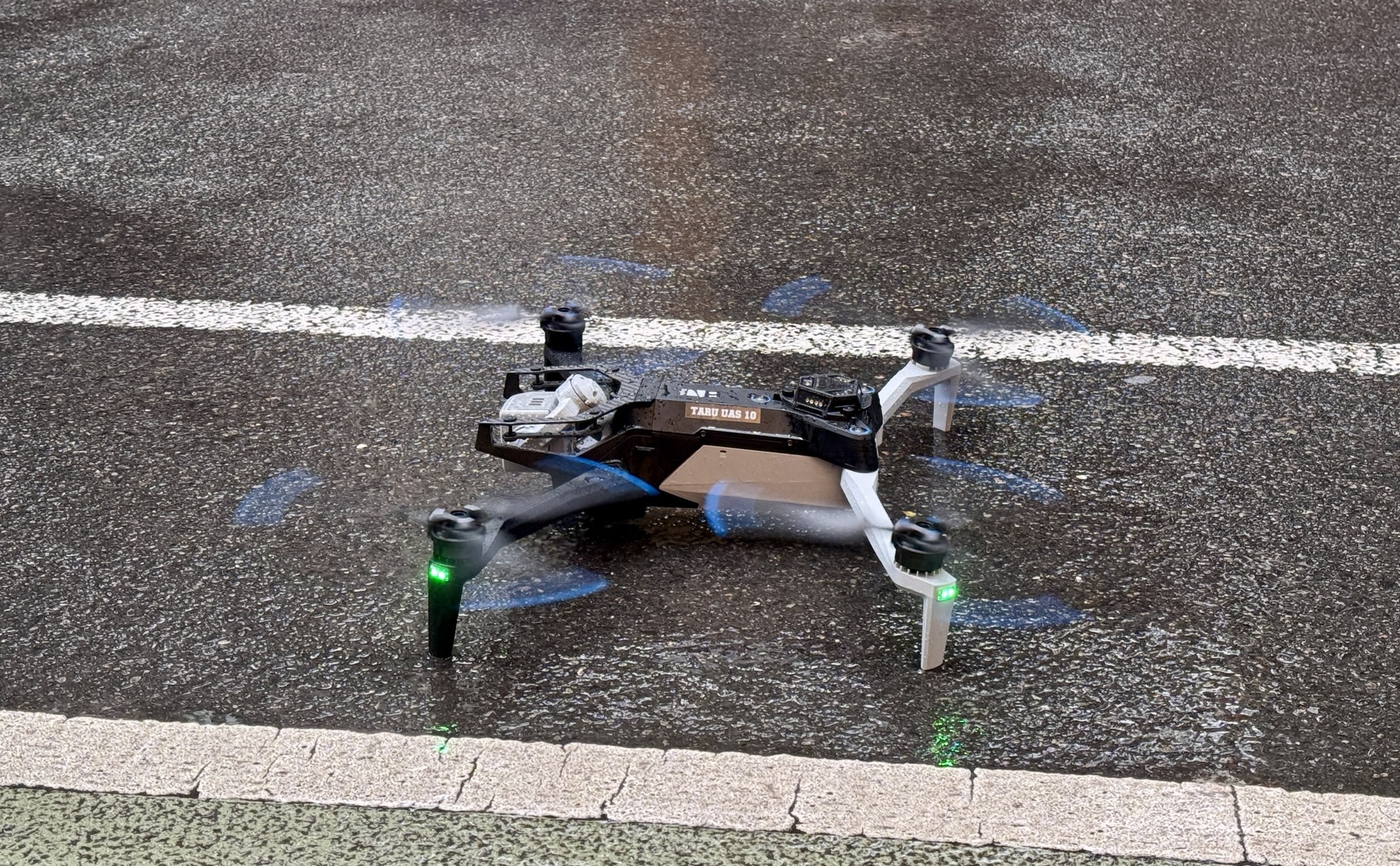 Skydio X10 on wet asphalt, blue-tipped propellers still and status lights green.
