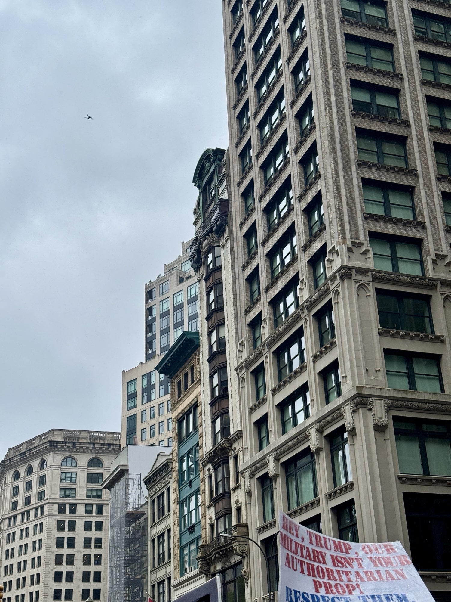 A tiny distant drone above Fifth Avenue near a protest banner on a building.