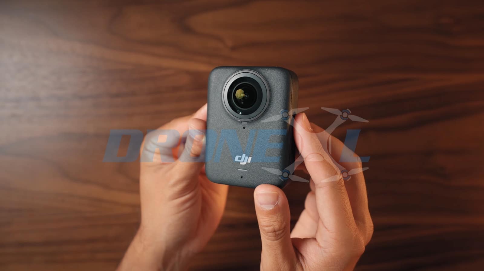 Hands cradling the square Osmo 360 above a walnut desk, front fisheye lens forward.