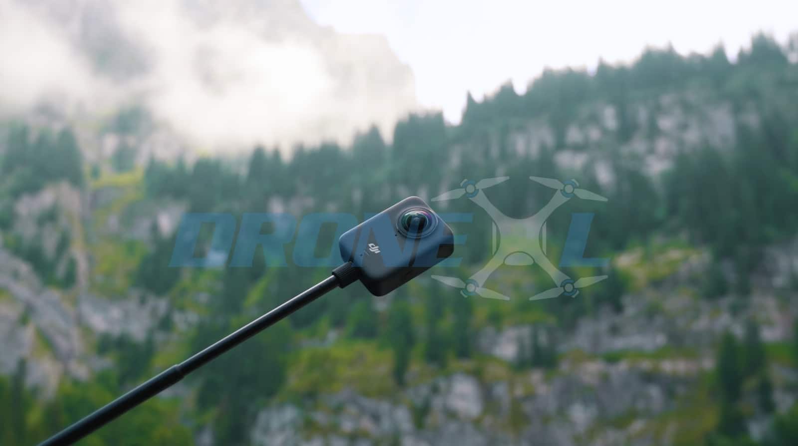 The 360 camera on a selfie stick against a misty forested cliff face.
