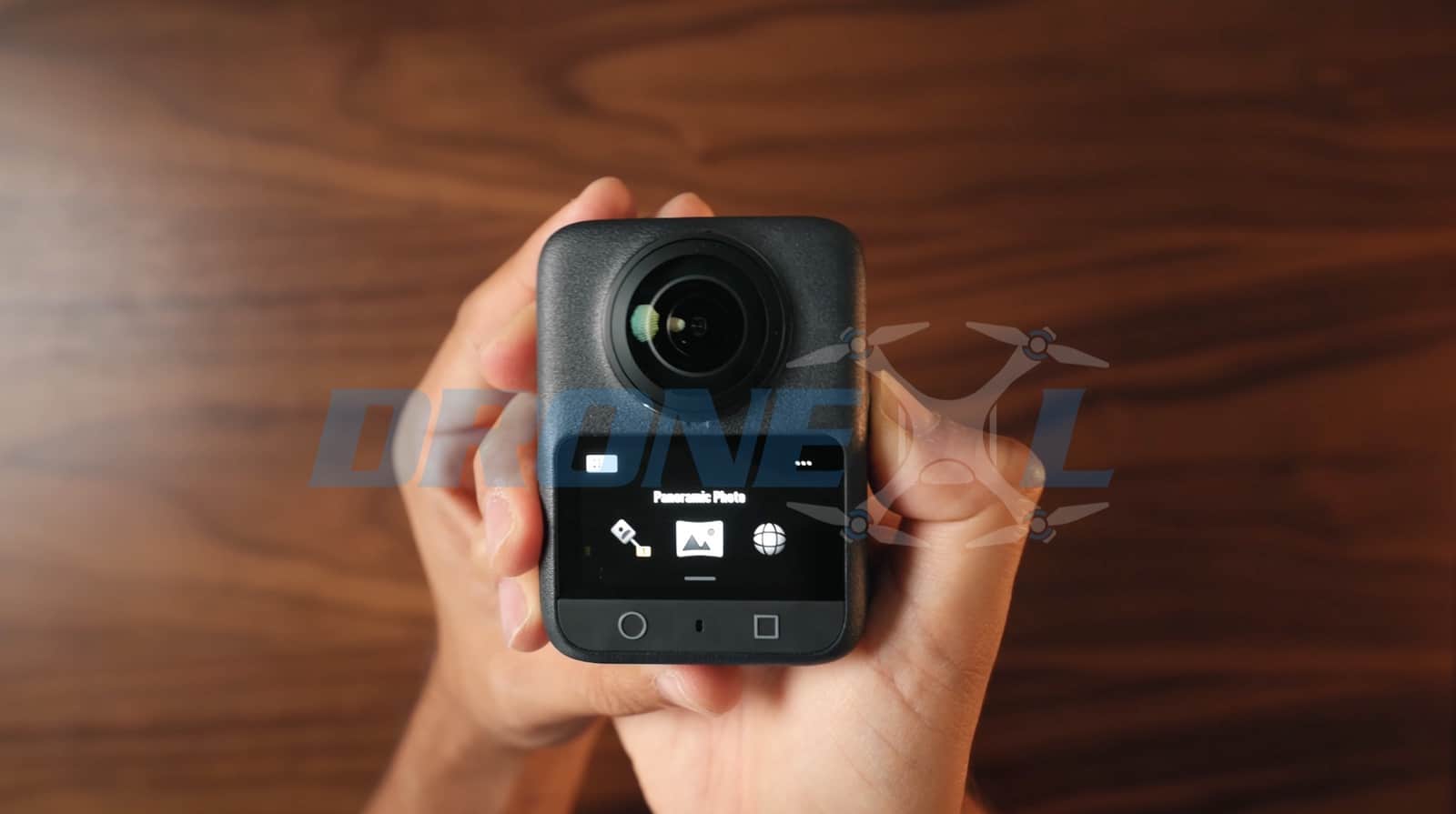 The OLED touchscreen showing panoramic photo mode icons as hands hold the camera.