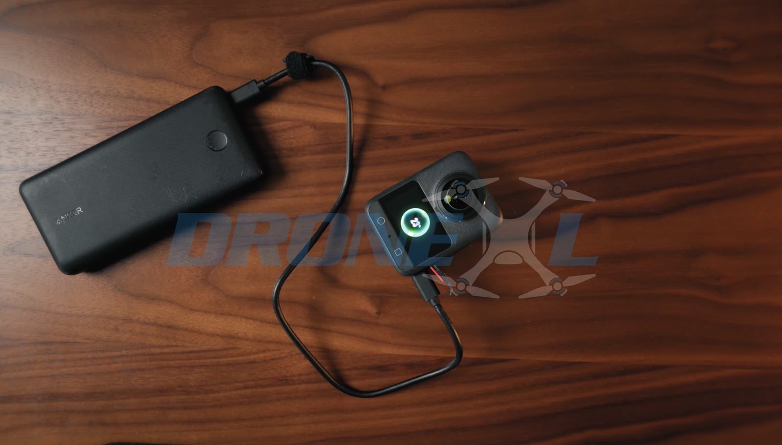 Camera charging from a black power bank over USB-C on the wooden desk.