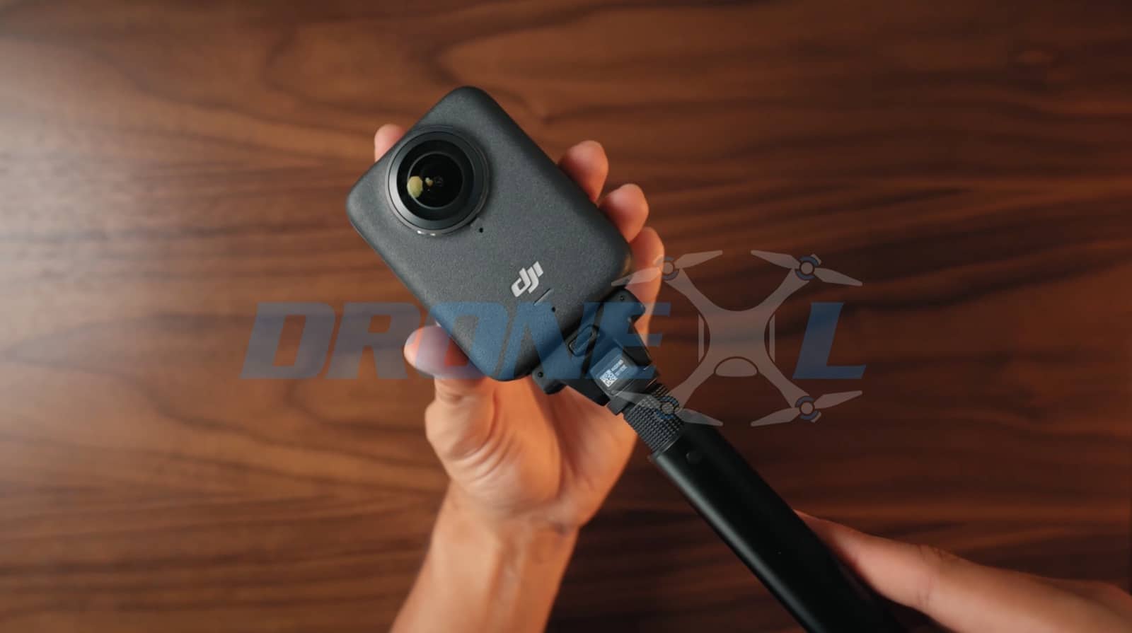Hands steadying the camera on the extended selfie stick over the desk.