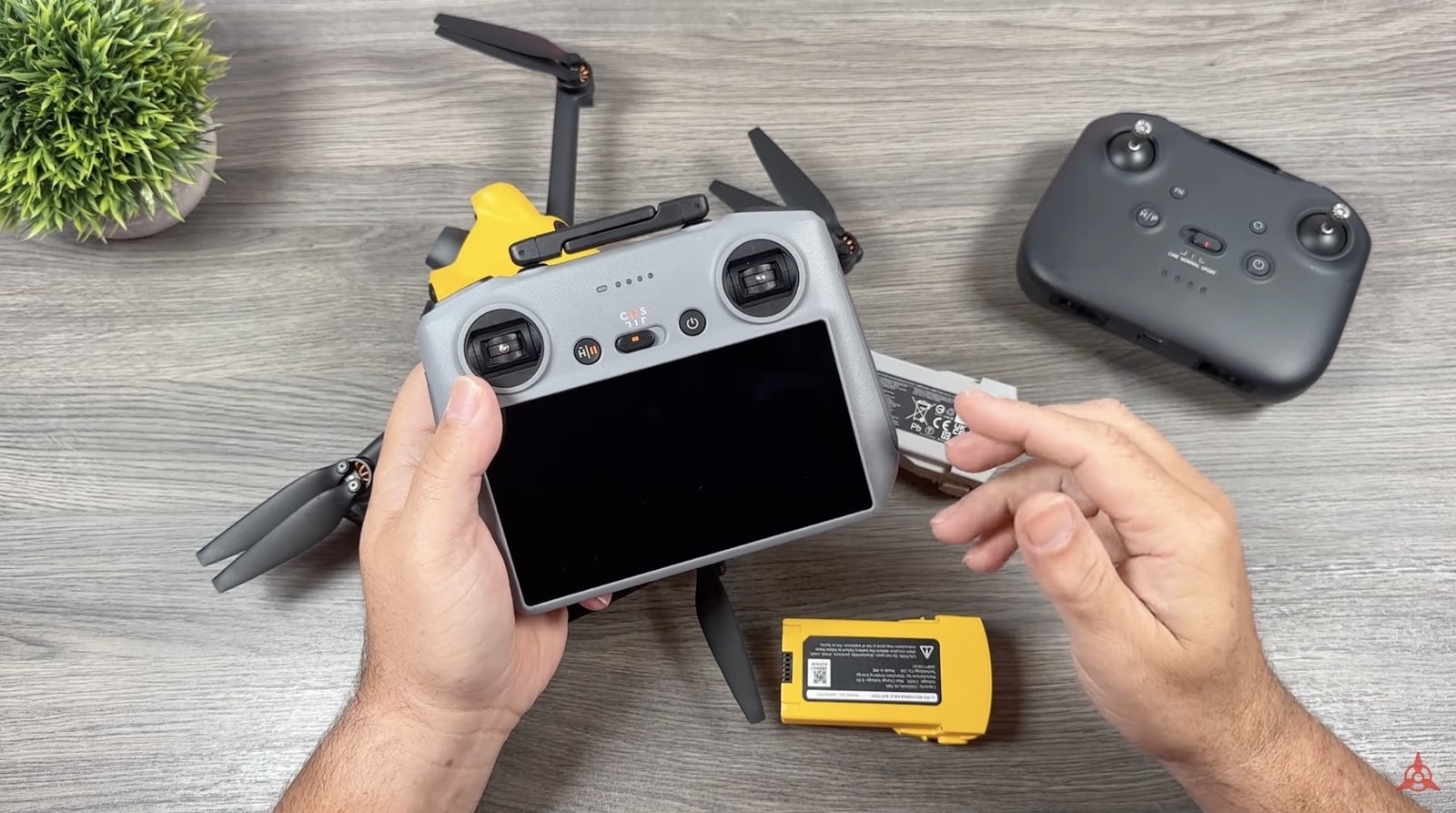 Hands hold a screen controller above the desk with the yellow drone below.