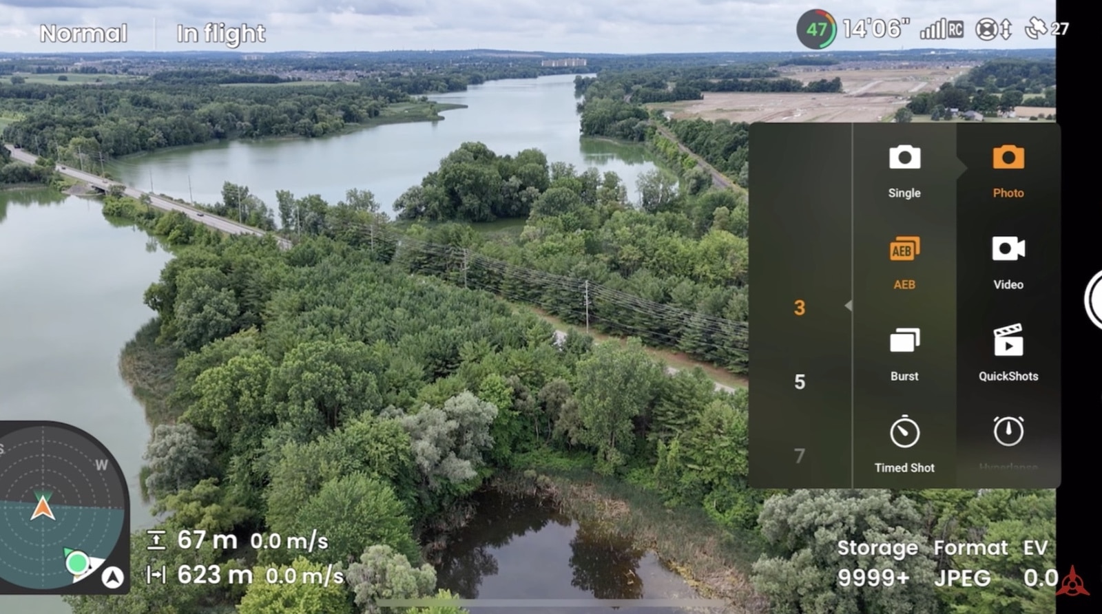 Flight view over a wooded river with the shooting mode wheel expanded.