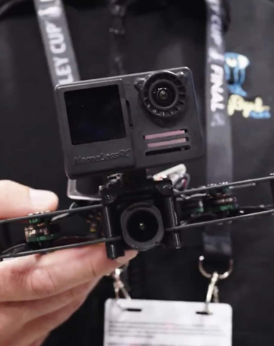 Hand holds a compact cinewhoop with an action camera mounted on top.