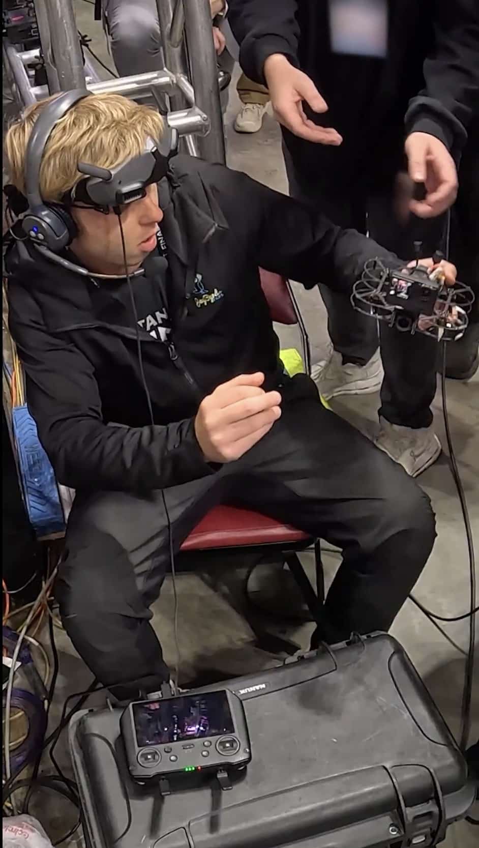 FPV pilot wearing goggles and a headset flies from a seat inside the arena.