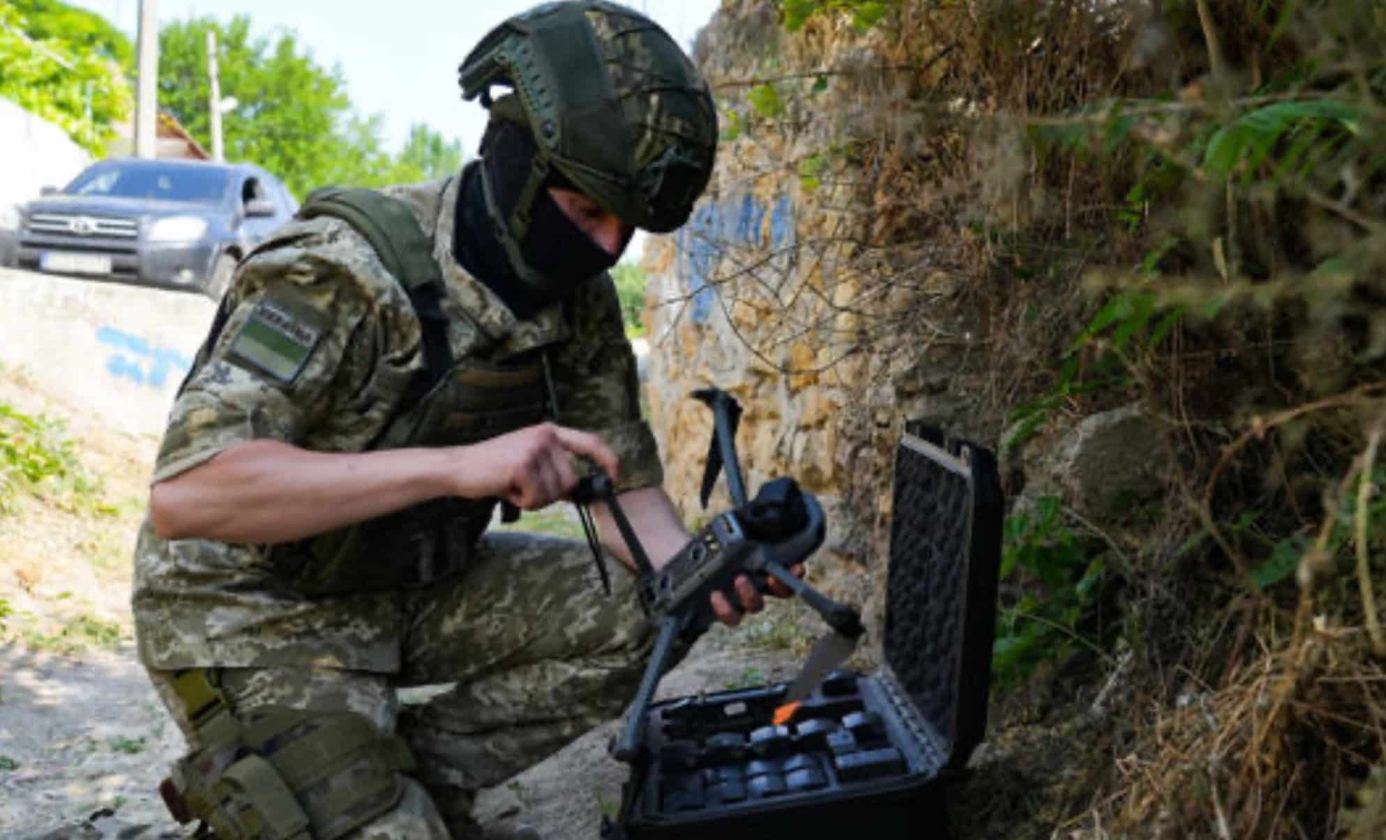 A masked Ukrainian soldier readies a folded Mavic beside its open carry case.