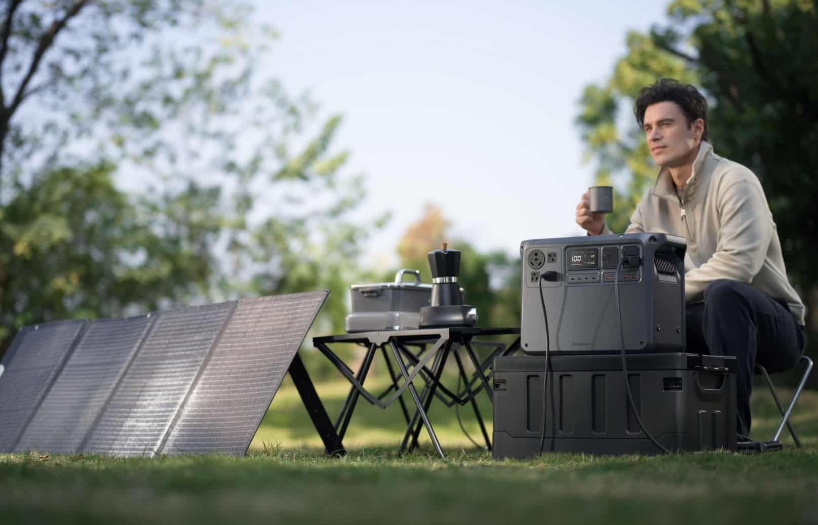 A man sits at a campsite table beside a folding solar panel and power station.