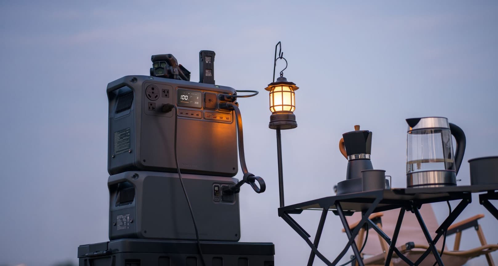 The station stacked with an expansion battery at dusk beside a lantern and kettle.