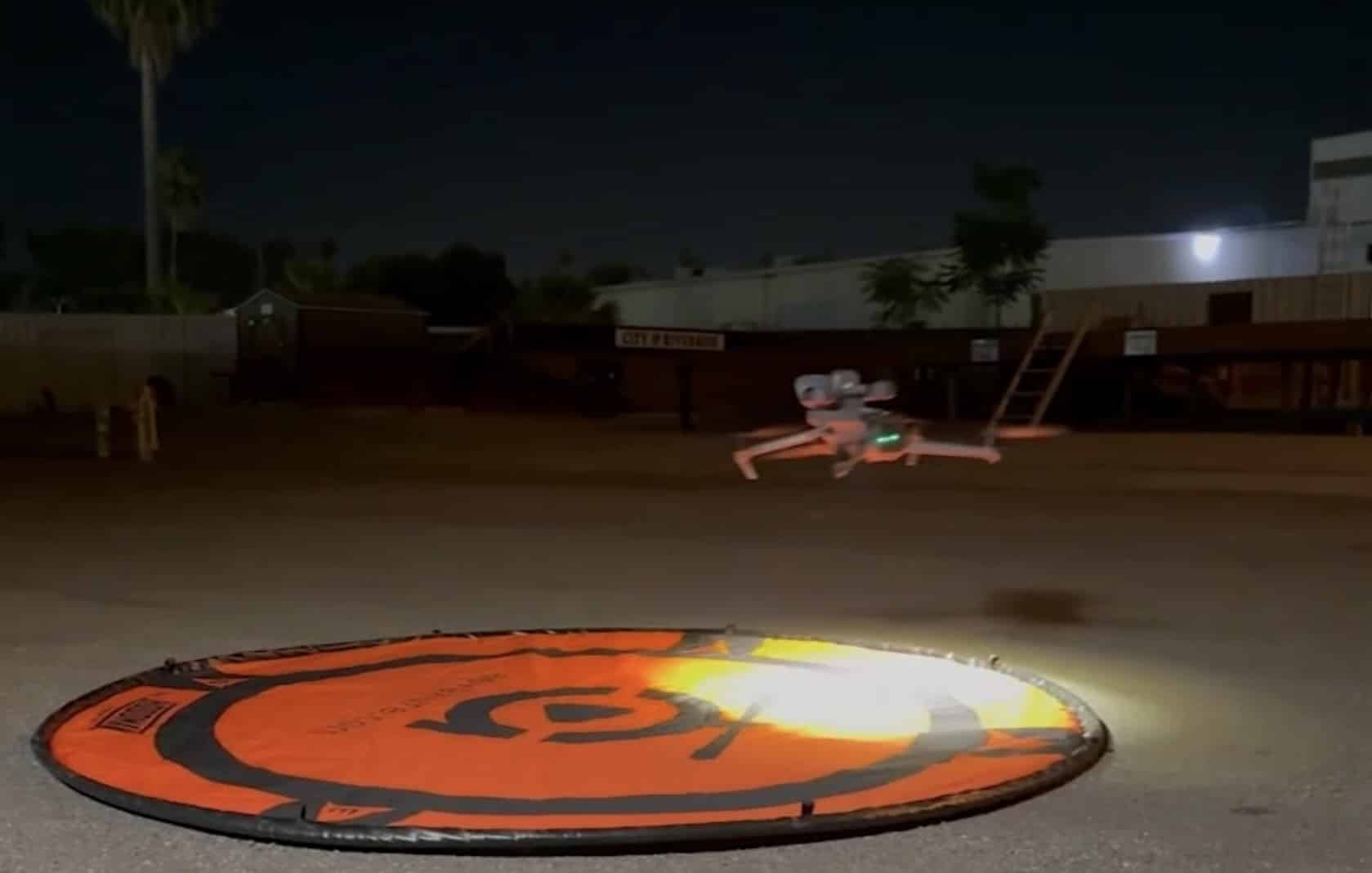 A police drone lifts off from an orange landing pad in a lot at night.
