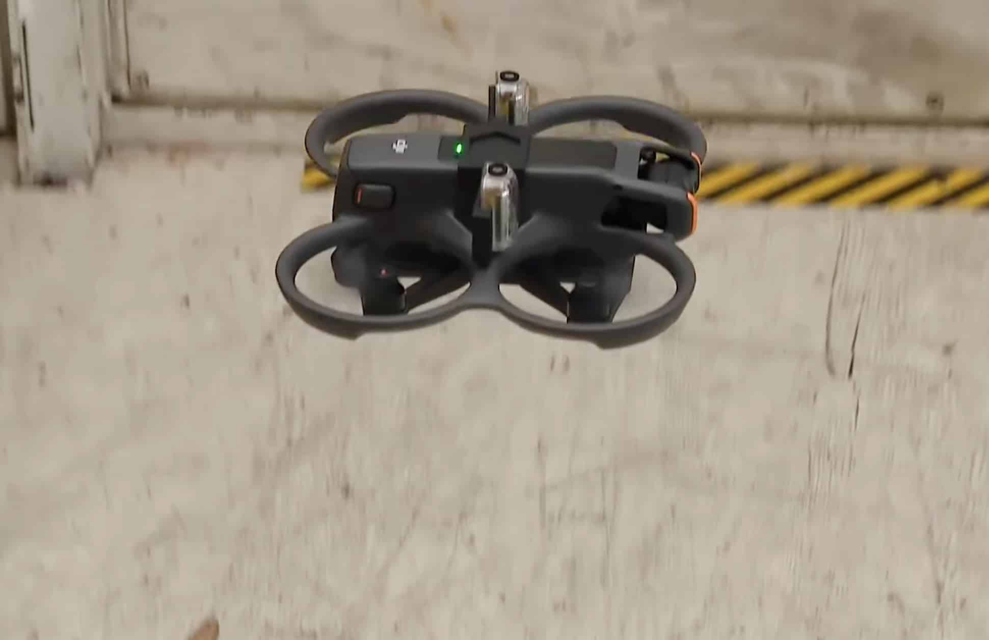 Close-up of a ducted DJI Avata hovering against a bare concrete wall.