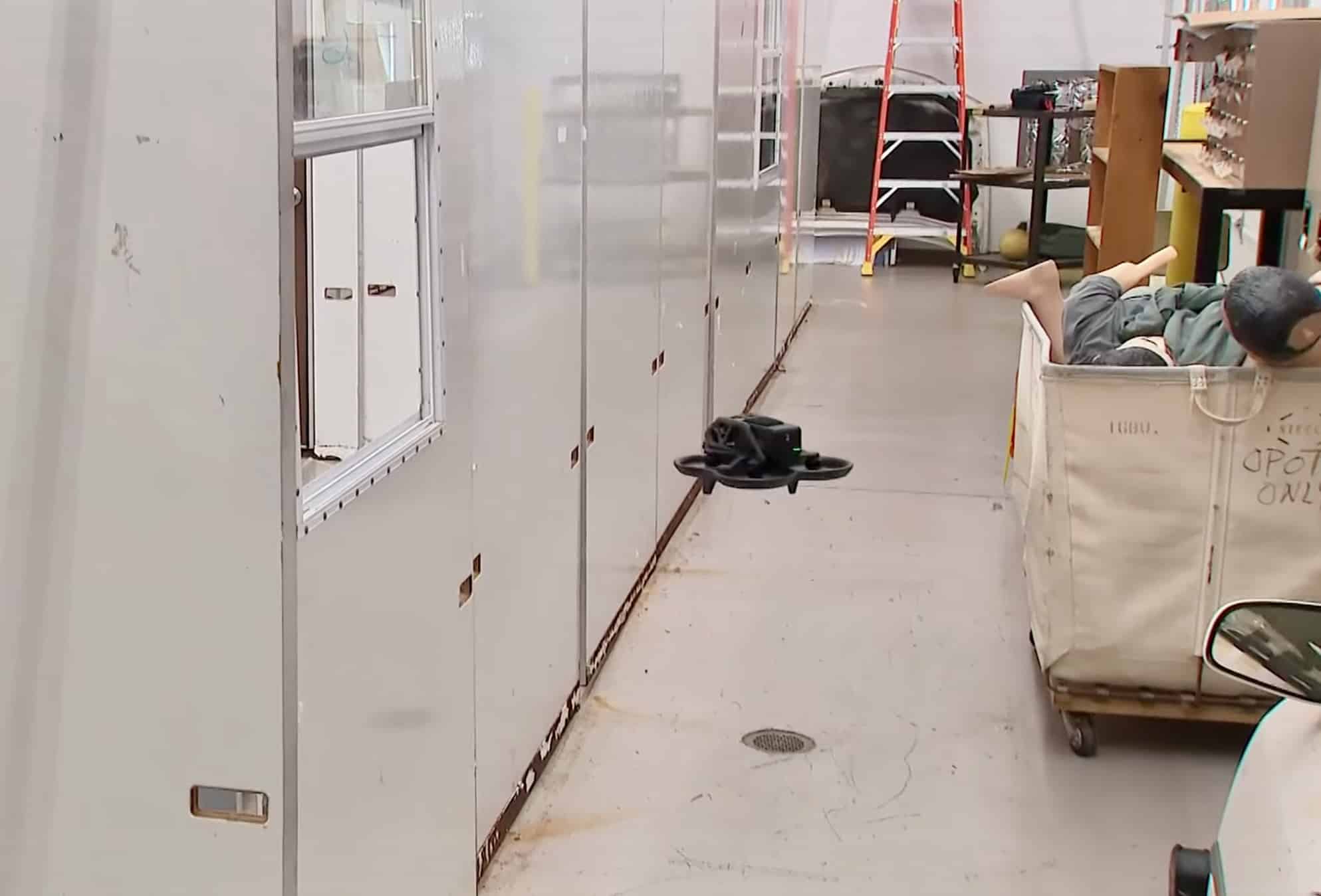 A small drone flies down a cluttered corridor inside the training building.