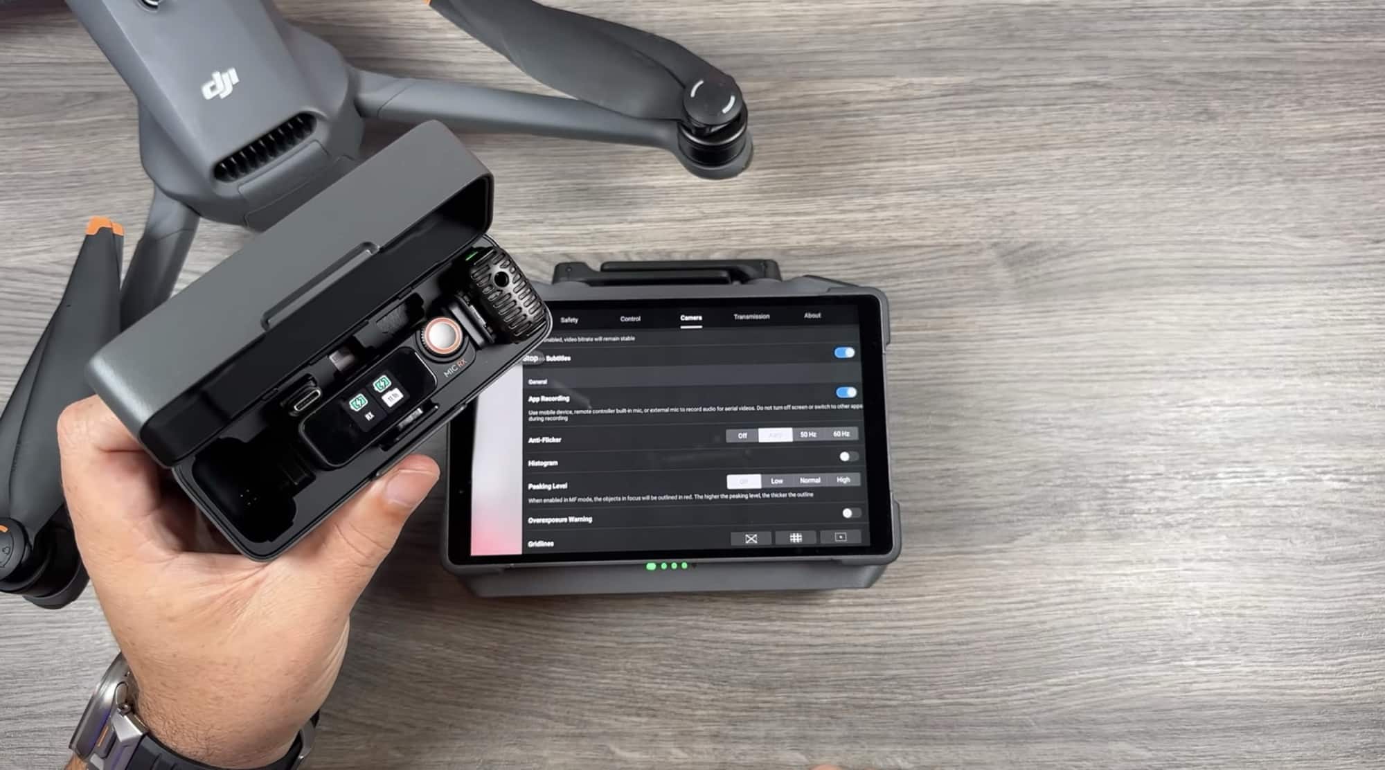 A hand holds the folded drone beside the controller showing a recording settings list.