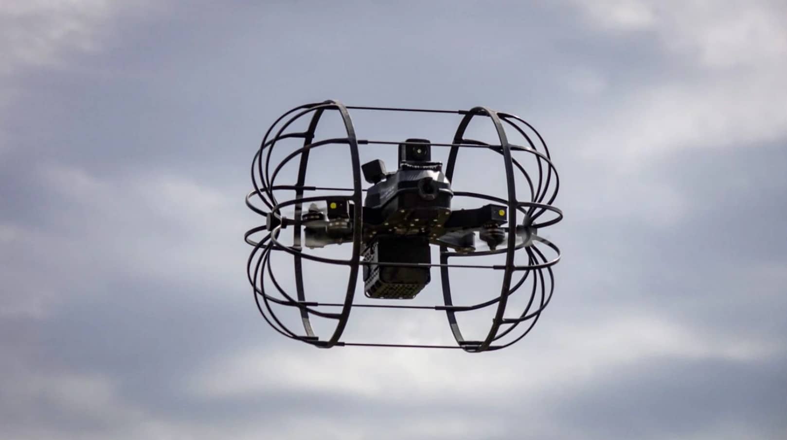 Rooster hybrid drone inside its round roll cage hovering against a cloudy sky.