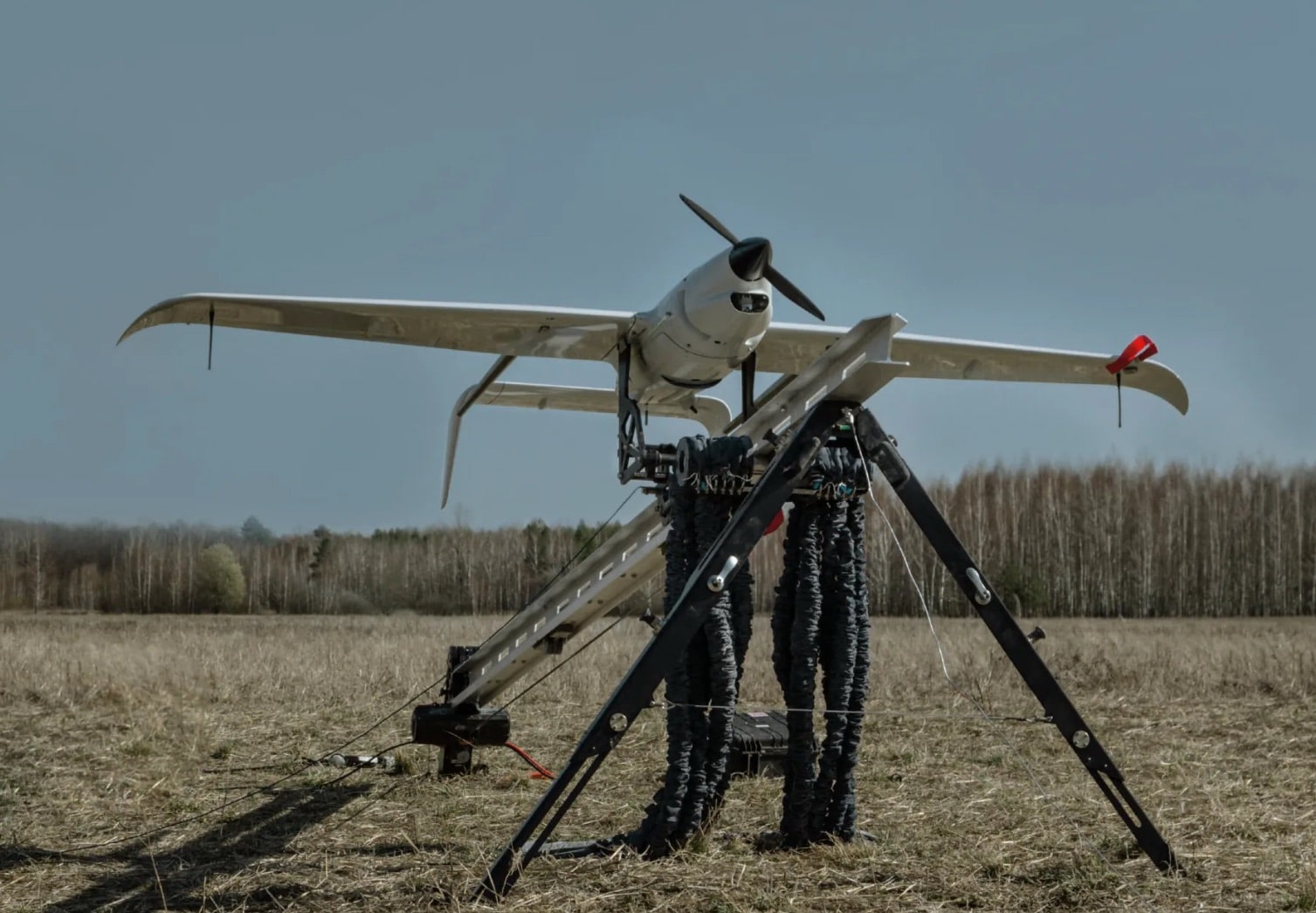 Fixed-wing reconnaissance drone loaded on its catapult launcher in a dry field.