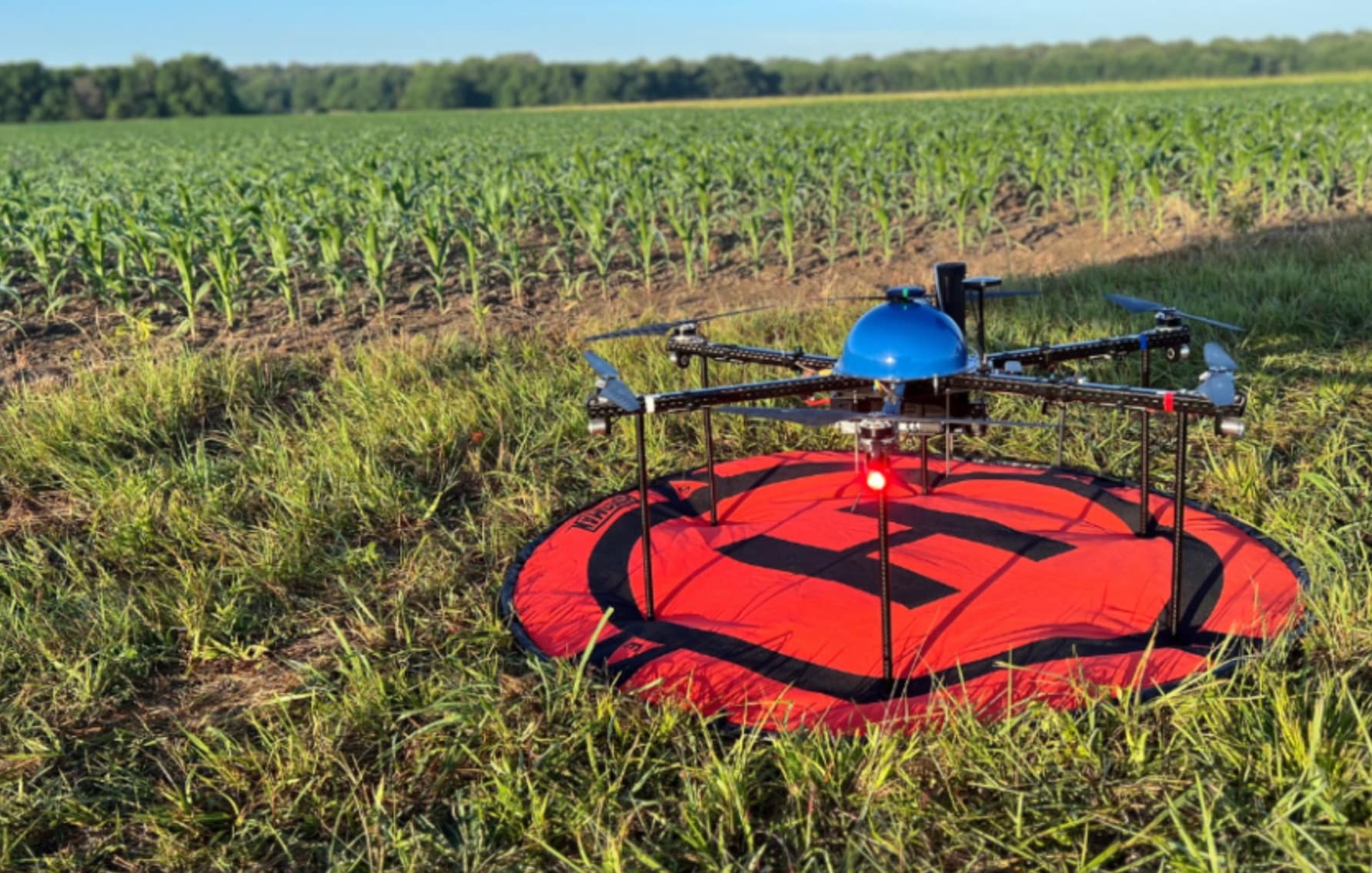 A delivery octocopter rests on a red circular landing pad in a green field.