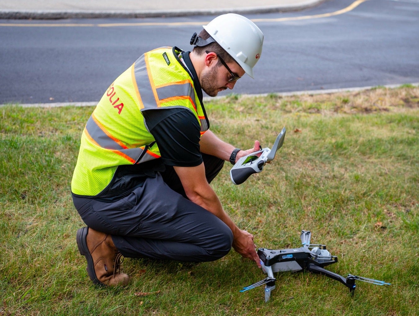 Utility technician in a hard hat sets up a quadcopter on a roadside verge.
