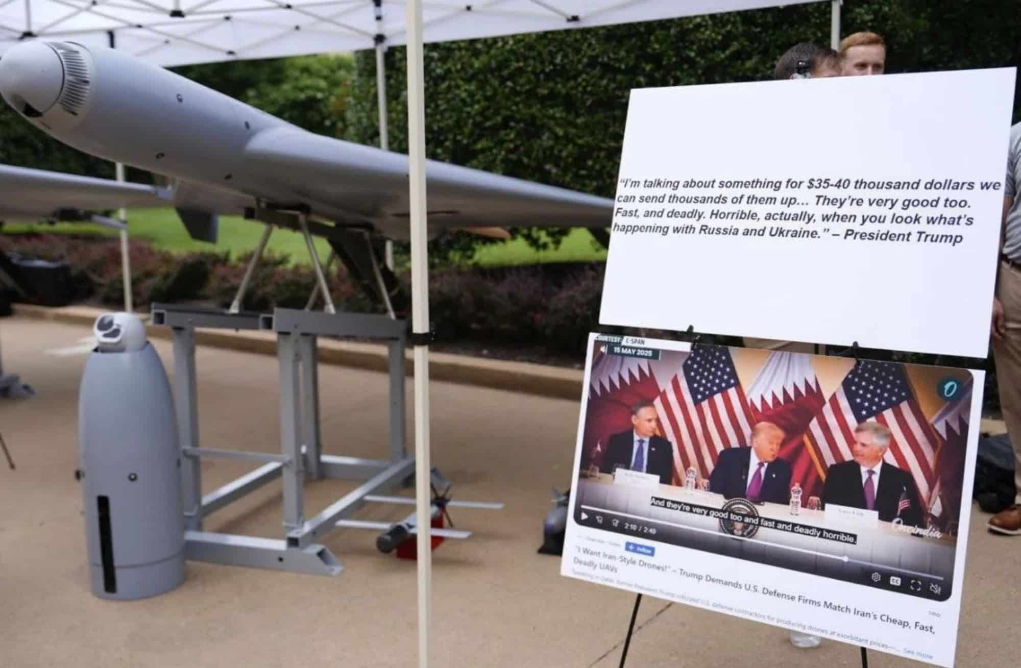 A grey delta-wing attack drone under a tent beside a board quoting the president.