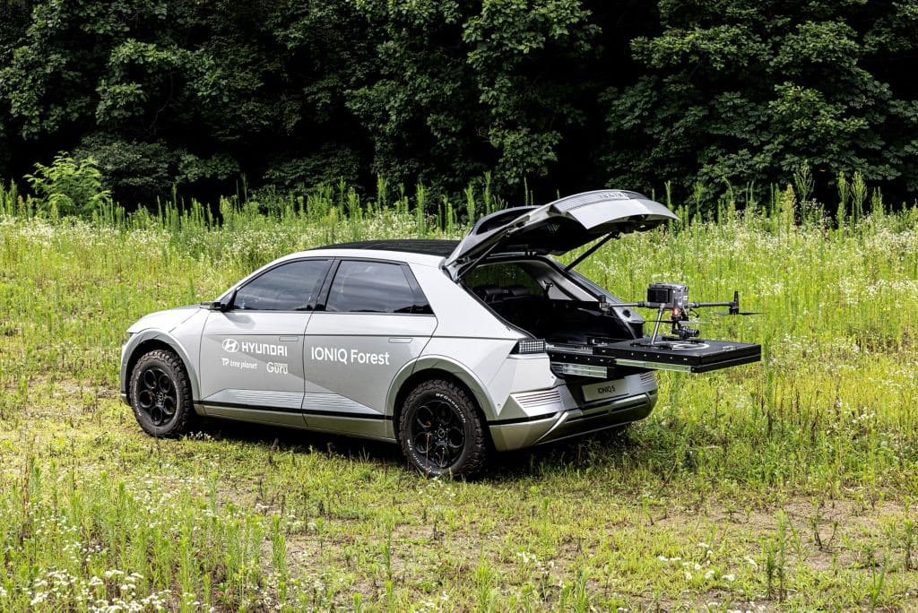 White Hyundai marked IONIQ Forest in a meadow with a drone on its tailgate platform.