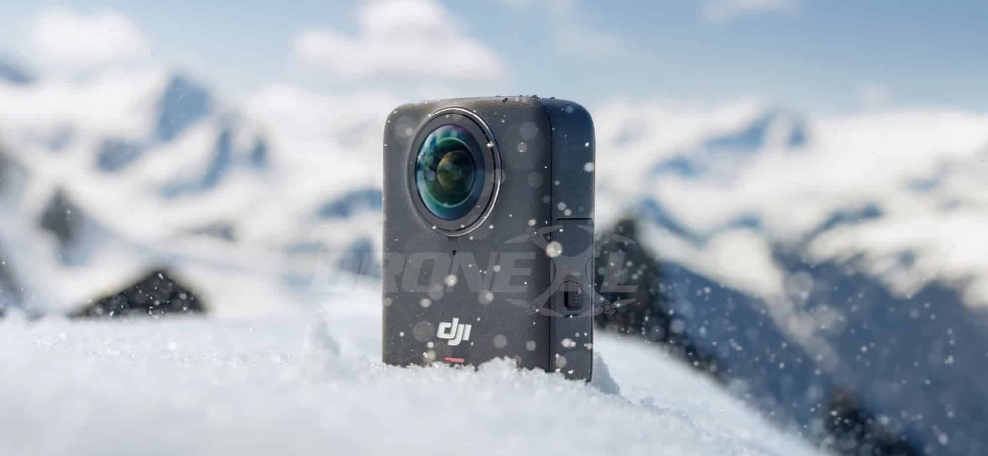 The black 360-degree camera stands upright in fresh snow before white peaks.