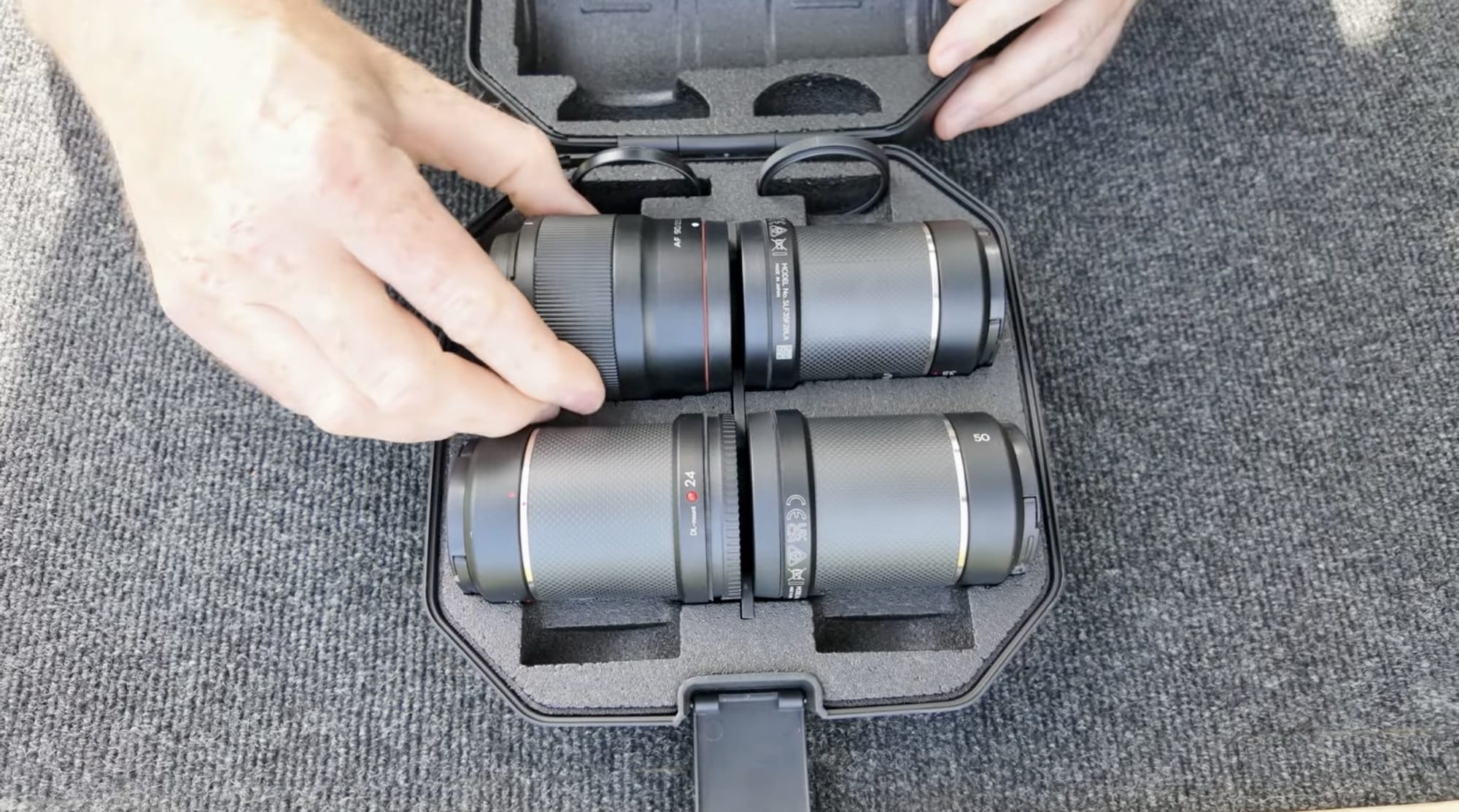 Hands lifting a DL lens out of the foam slots of its case.