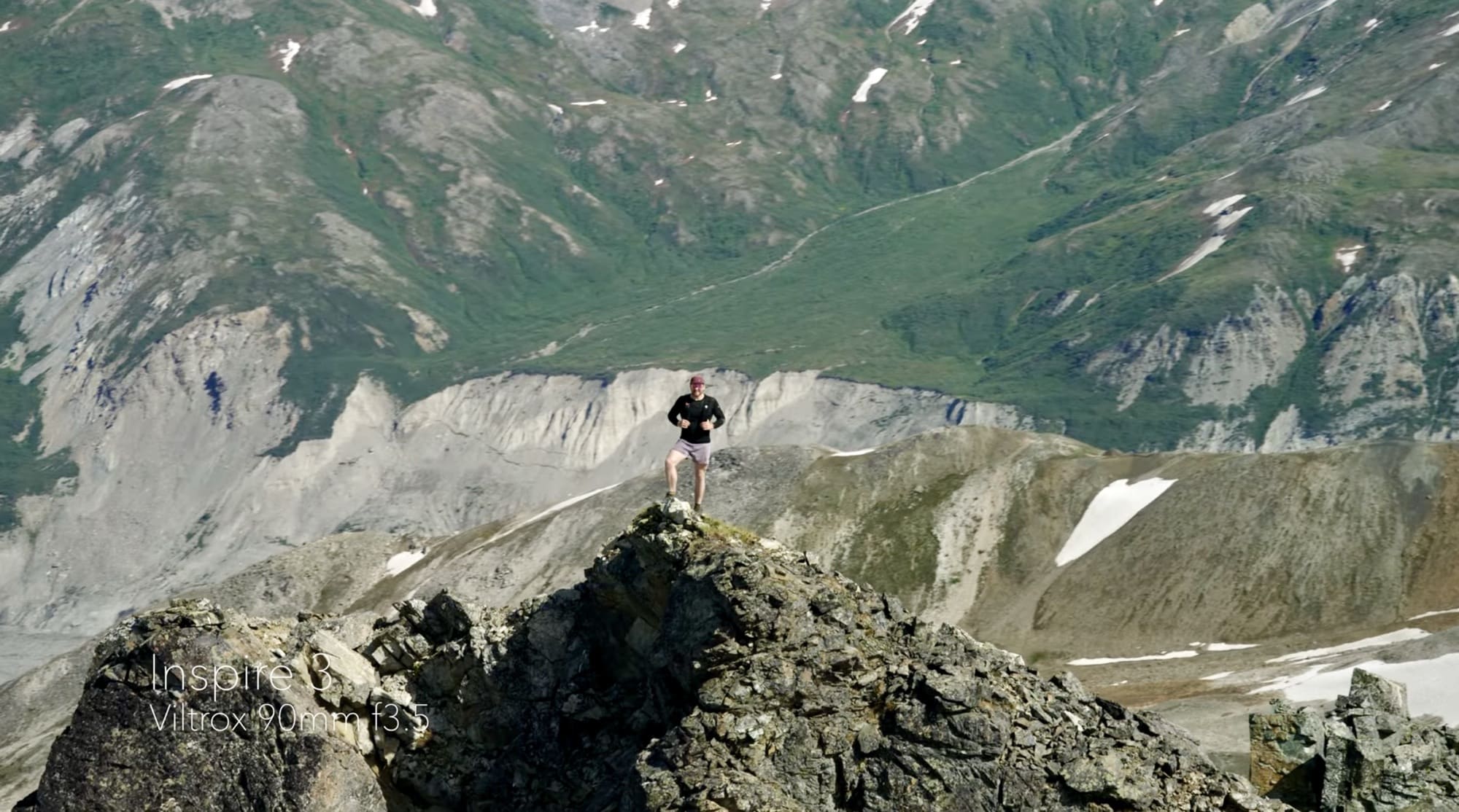 Distant figure standing on a rocky ridge above a wide glacial valley.