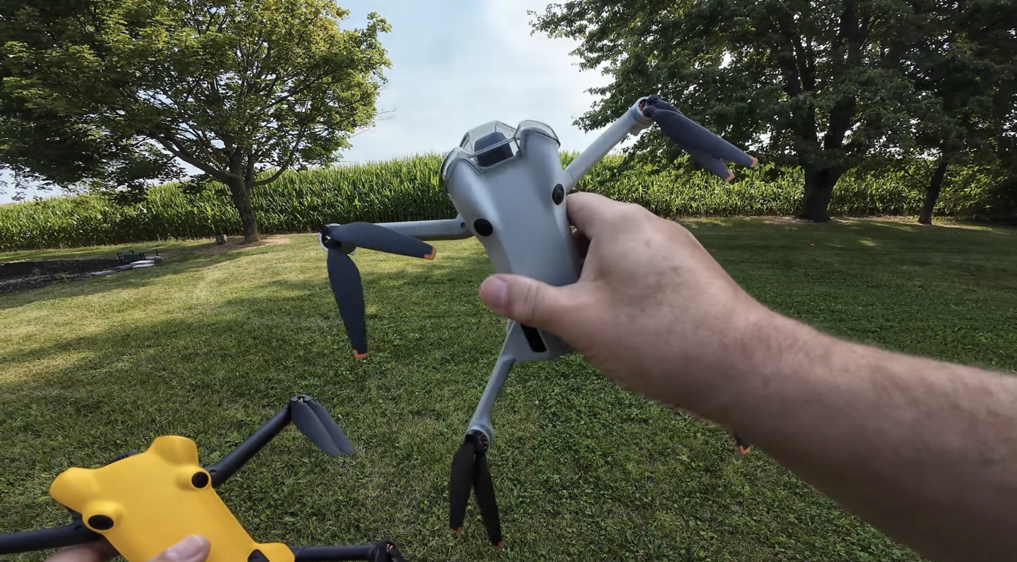 A hand holds the folded DJI Mini 4 Pro over the same stretch of grass.
